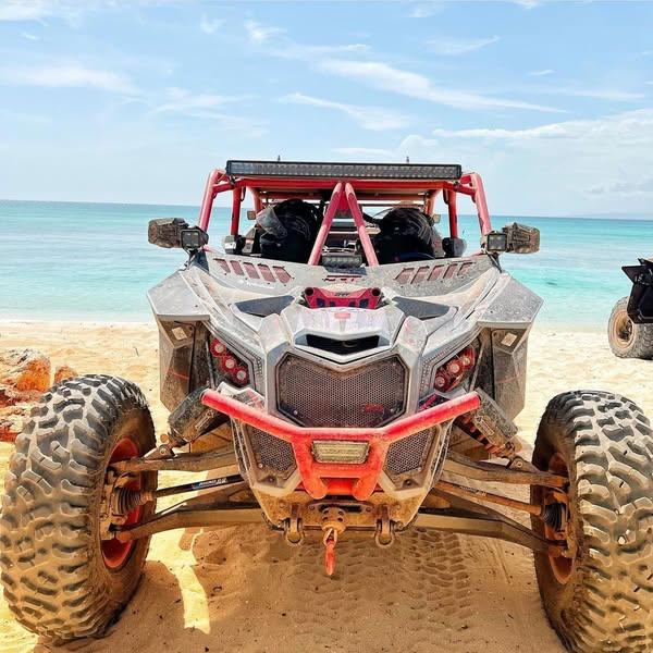 DRT wind diffuser installed across the lower A-pillars of a Can-Am Maverick X3 on a beach ride; custom red cage, mud and other accessories shown.