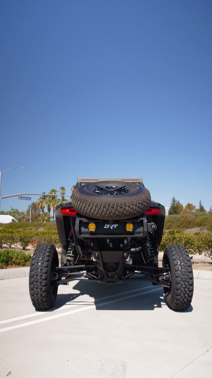Rear view of DRT Desert Runner fixed tire carrier installed on a Polaris RZR Pro Series build, with spare tire and optional rear lights shown; tire and lights sold separately.