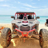 DRT wind diffuser installed across the lower A-pillars of a Can-Am Maverick X3 on a beach ride; custom red cage, mud and other accessories shown.