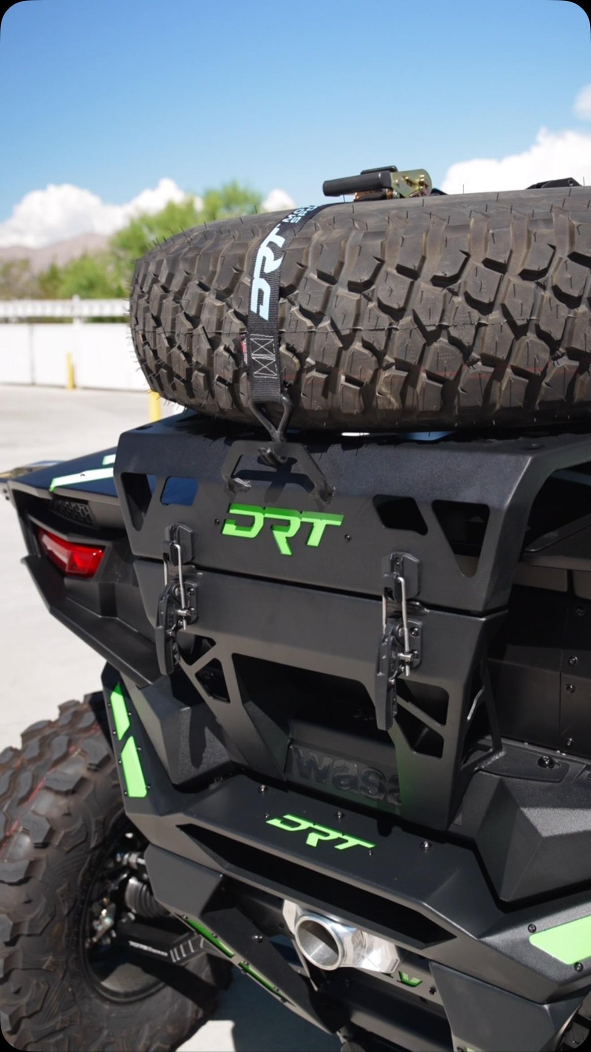 DRT tire carrier installed on a Kawasaki Teryx H2, showing the spare-tire tie-down and twin trigger latches; custom green accents and other accessories shown.