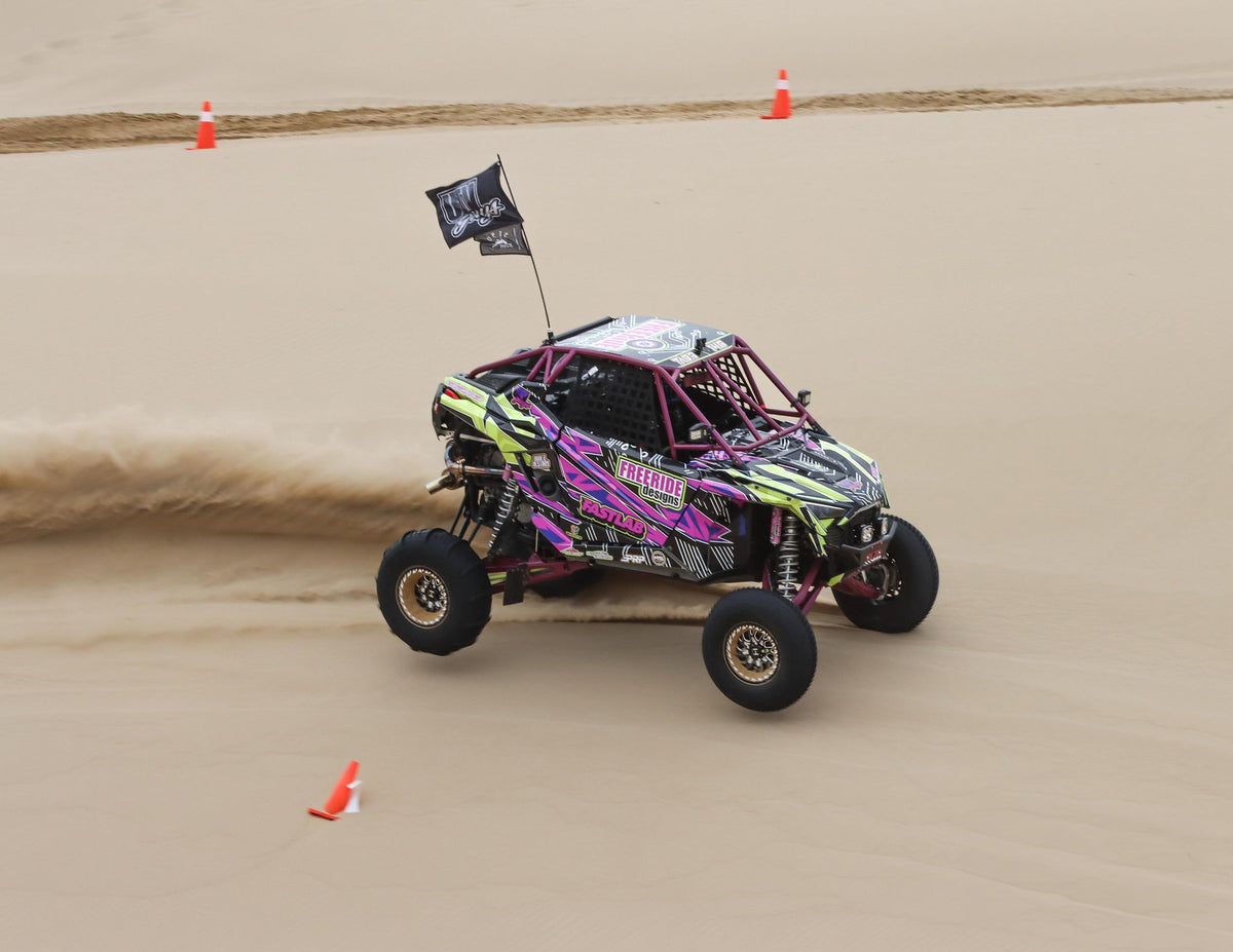 Hostile H333 Glamis Beadlock wheels on a purple and green Polaris RZR Pro R turning across the dunes. Hostile manufacturer gallery.