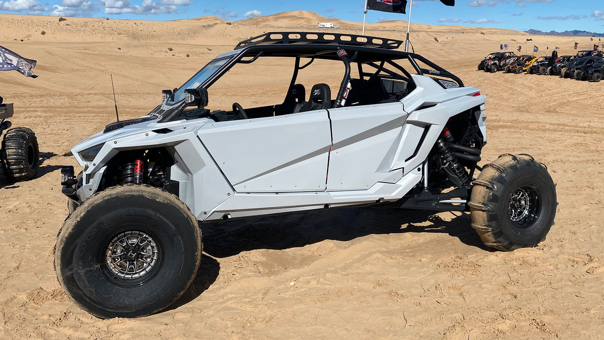 Hostile HF22 Rival rear wheels on a white Polaris RZR Pro R in the dunes; front wheels use a beadlock setup. Hostile manufacturer gallery.