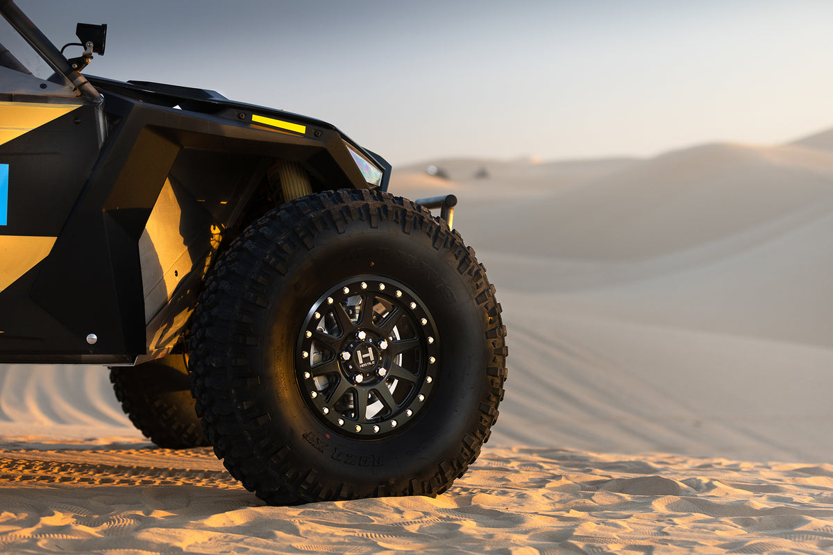 Installed Hostile HF23 Baja Beadlock wheel on a Polaris RZR Pro R at sunset in the dunes. Hostile manufacturer gallery.