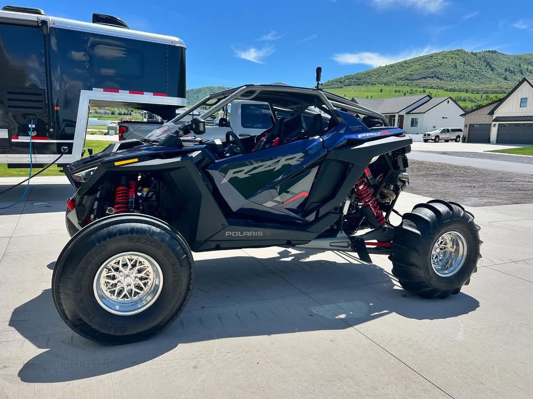 Packard Impact polished-barrel wheels installed on a blue Polaris RZR Pro R with front sand tires and rear paddles. Real build photo from Packard Performance; cap and setup details may vary.