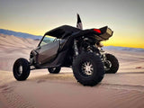 Can-Am Maverick X3 on sand dunes at sunset with Packard Wishbone silver-center, black-barrel non-beadlock wheels and rear paddle tires.