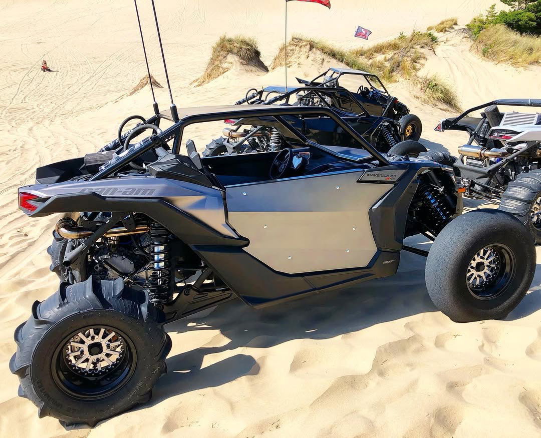Can-Am Maverick X3 on the dunes with Packard Wishbone silver centers and black non-beadlock barrels. Real Packard build photo; front sand tires and rear paddles shown, sold separately.